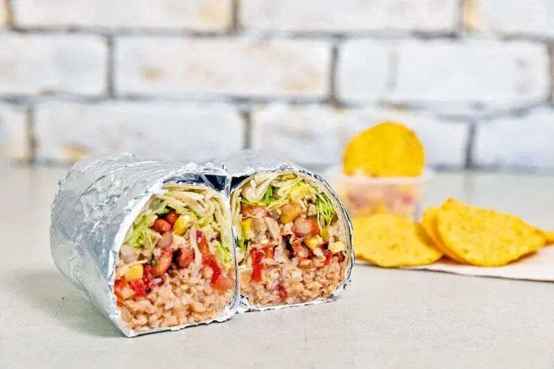 Burrito cut in half on counter with chips in the background