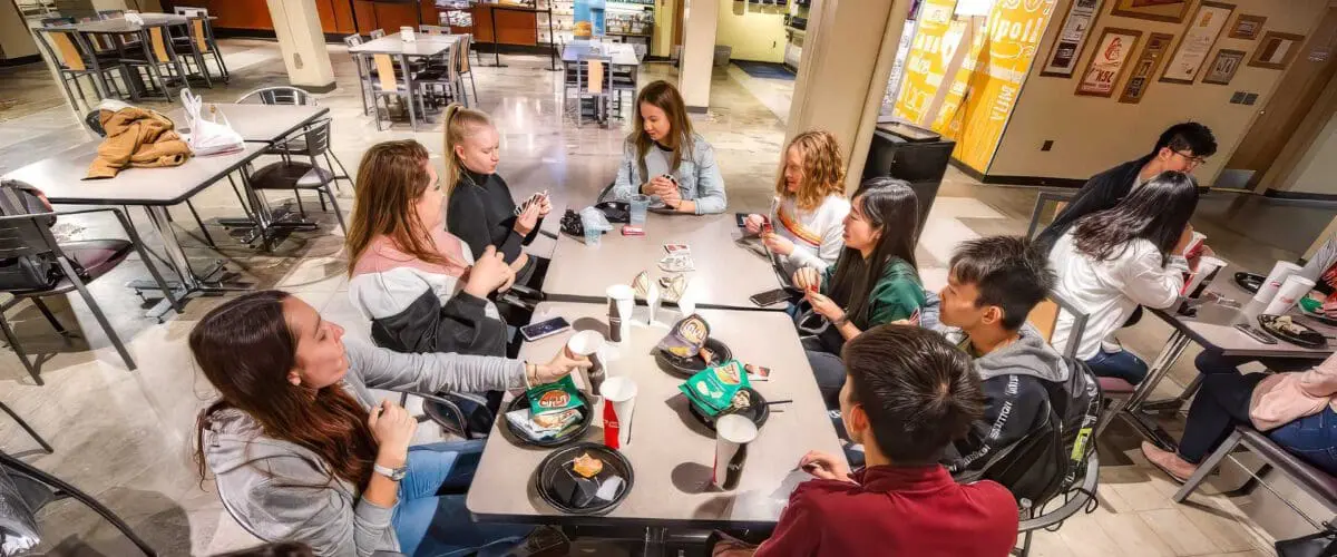 Students sitting around tables, eating and playing card games