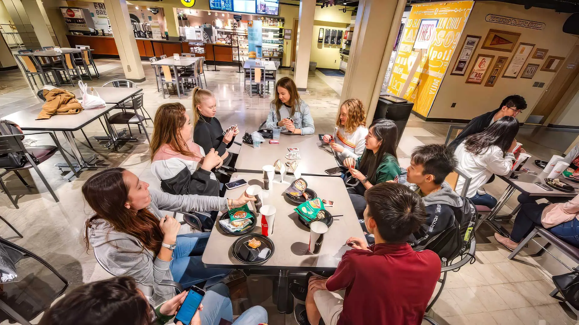 Students sitting around tables, eating and playing card games