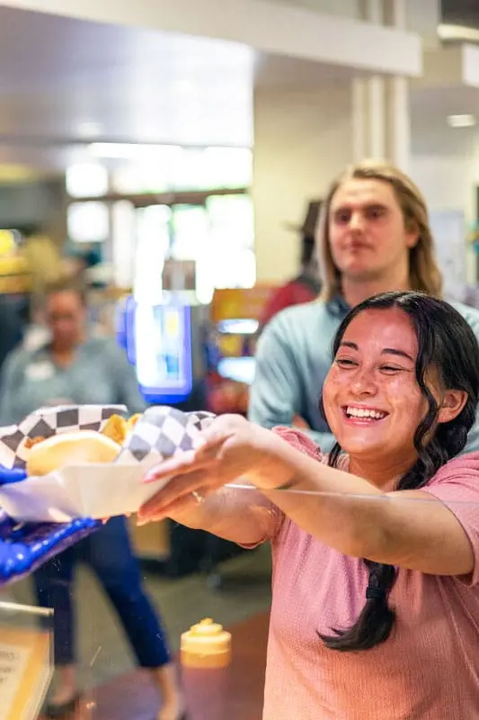 Student smiling while being passed a plate of food